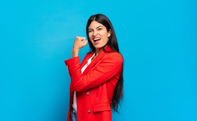 young hispanic businesswoman feeling happy, satisfied and powerful, flexing fit and muscular biceps, looking strong after the gym