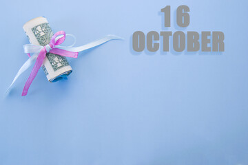 calendar date on blue background with rolled up dollar bills pinned by blue and pink ribbon with copy space. October 16 is the sixteenth day of the month