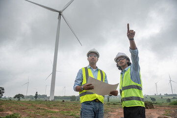 Naklejka premium Two engineers working and holding the report at wind turbine farm Power Generator Station on mountain,Thailand people