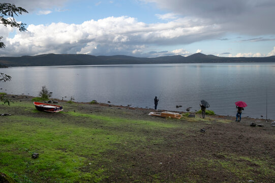 Two people looking at a person fishing in the rain, Lake Bracciano, Lazio, Italy
