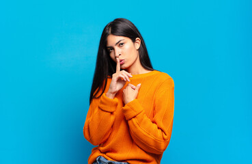 young pretty hispanic woman looking serious and cross with finger pressed to lips demanding silence...