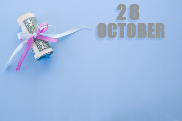 calendar date on blue background with rolled up dollar bills pinned by blue and pink ribbon with copy space. October 28 is the twenty-eighth day of the month