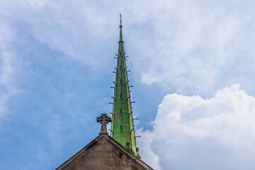 Copper art deco church spire and Celtic cross on top of church against beautiful cloudy blue sky