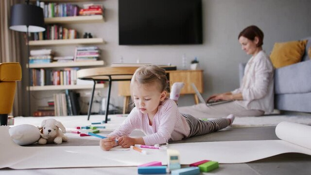 Girl at home drawing a picture while her parents are working. Homeoffice concept.