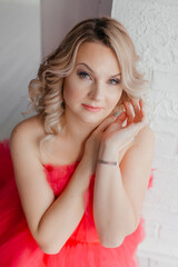 Obraz na płótnie Canvas A young blonde woman in a beautiful puffy pink dress. A beautiful woman in a light-colored photo studio. Ball Gown. Portrait of a girl with makeup and hairstyle