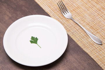 Single one parsley green leaf on white empty plate and fork on table. Diet, fasting, vegan, vegetarian, healthy food concept - Powered by Adobe