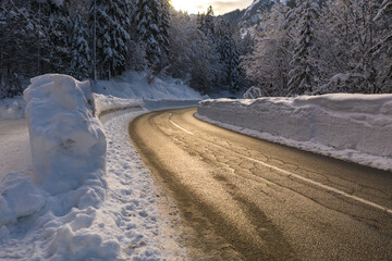 Driving on a snowy winter road through a forest in nature with sun shining.