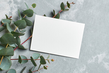 Stylish wedding invitation card mockup with eucalyptus twigs on grey stony background