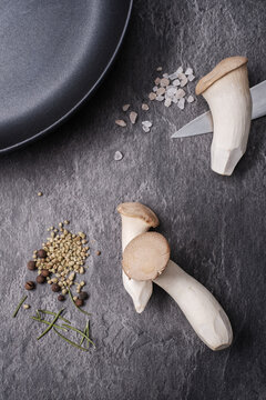 Knife, pan and fresh royal oyster mushrooms or eringo with rosemary spice as ingredients for healthy gourmet meal on a granite table.	