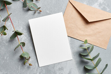 Wedding invitation card mockup with envelope and eucalyptus branches on grey concrete background
