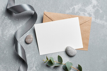 Wedding invitation card mockup with envelope, silver ribbon and eucalyptus on grey concrete...