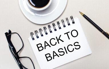 Glasses, a white cup of coffee, a white notebook with the words BACK TO BASICS and a ballpoint pen lie on a light background. Flat lay. View from above.