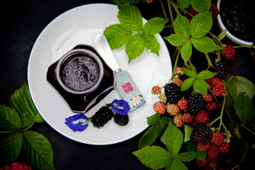 Homemade Blackberry Jam in a Glass Jar on White Plate Decorated with Fresh Blackberry Branches
