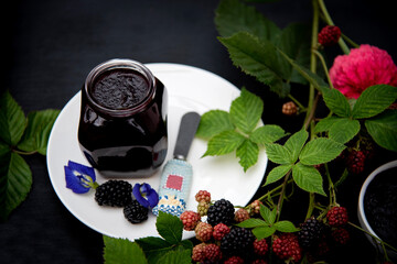 Homemade Blackberry Jam in a Glass Jar on White Plate Decorated with Fresh Blackberry Branches