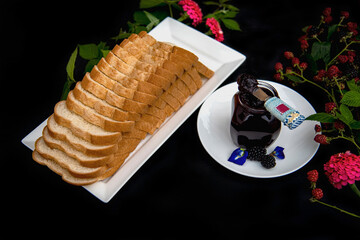 Sliced Bread Loaf on White Plate with  a Glass Jar of Homemade Blackberry Jam on Black Background