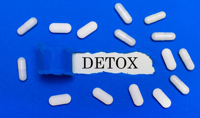 White pills lie on a beautiful blue background. In the center is white paper with the inscription DETOX. Medical concept. View from above.