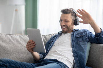 Cheerful man having video call with friends, using digital tablet
