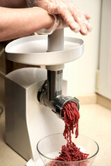  The process of grinding meat into minced meat in a meat grinder. Gloved hands push the meat into the meat grinder. Selective focus.