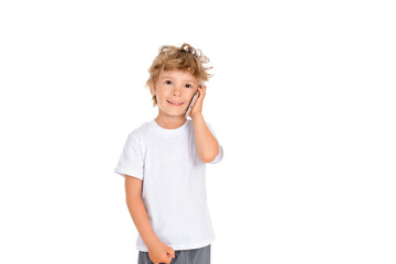 A cute white boy with an interesting hairstyle is standing on a white isolated background and talking on a cell phone (smartphone) and smiling affably. Dressed in a white t-shirt