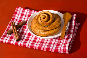 Freshly baked cinnamon bun stuffed with spices and cocoa on a red table with a tough shade. Sweet homemade cakes. Kanelbullar is a Swedish dessert.