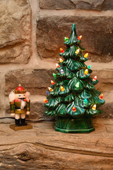 Lighted ceramic Christmas tree and nutcracker soldier figurine on wood barn beam mantle on stone...