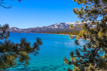  a stunning shot of the vast clear blue lake water with snow capped mountain ranges and lush green...
