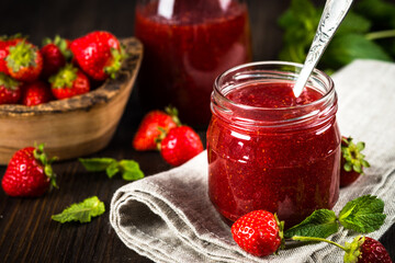 Strawberry jam in the glass jar with fresh berries at wooden table.