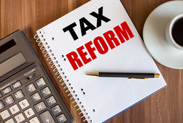 TAX REFORM written in a white notepad near a calculator and a cup of coffee on a dark wooden background