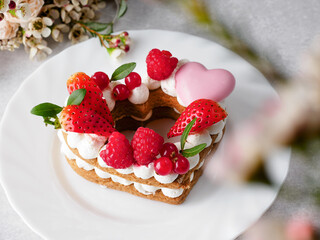 The heart-shaped layer cake is decorated with fresh berries, chocolate and flowers. Cake with fresh strawberries, raspberries and red currants. Dessert with red berries. Copy space.  Valentine's Day.