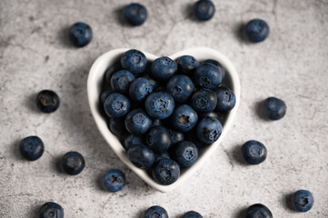 Fresh blueberries in a small heart shaped plate on a concrete background. Healty lifestyle concept. Vitamins