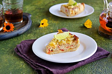 Portion of open unsweetened shortcrust pastry pie with tuna, sweet red pepper and cheese on a white plate on a green concrete background. Fish pie recipes.