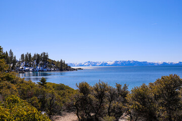  a stunning shot of the vast clear blue lake water with snow capped mountain ranges and lush green...