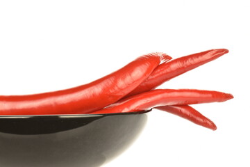 Several red juicy, hot peppers with a black ceramic plate, close-up, isolated on white.