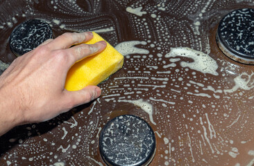 Cleaning and washing the hob. Removing grease from a gas stove. Hand with cleaning sponge and foam...