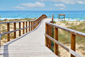 Obraz premium Wooden boardwalk leading through sandy dunes to Sea. Spain