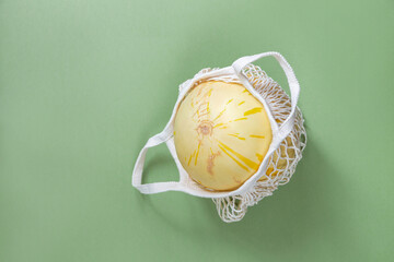 Ripe honeydew melon in eco-friendly cotton mesh on dark pistachio background close up. Copy space.Top view.