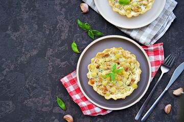 Portion mini tart with chicken, zucchini and fried onions on shortcrust pastry with sour cream and eggs filling on a clay plate on a dark concrete background. Savory pastry recipes.