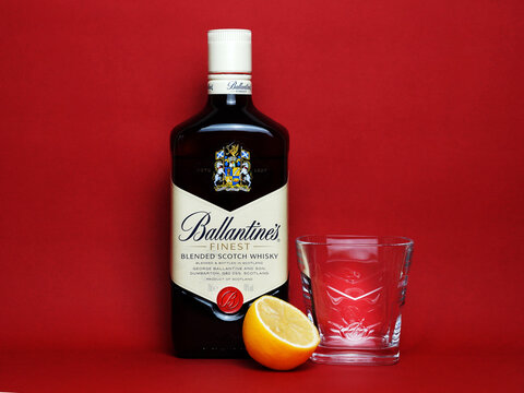 Ballantine's scotch whiskey bottle, glass and half lemon on red background