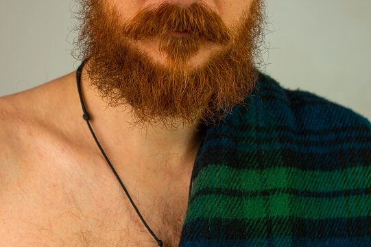Irish red bearded man in traditional green kilt celebrates St. Patrick's Day. Handsome scottish guy portrait with beard and mustache drinks whiskey in pub. 17 March cultural parade celebration Ireland