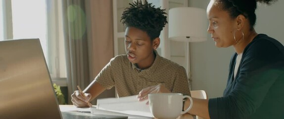 African American Black mother giving high five to son, helping him with homework. Distance learning from home during COVID-19 coronavirus pandemic, stay home concept. Shot with 2x anamorphic lens