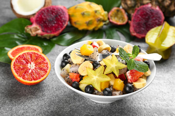 Delicious exotic fruit salad and ingredients on grey table