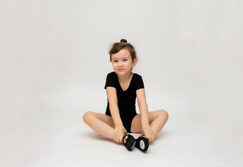 Fototapeta na wymiar little gymnast girl in a black uniform does a stretch on a white background with a place for text
