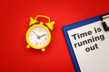 Time is Running Out - phrase on paper with yellow alarm clock aside on red background.