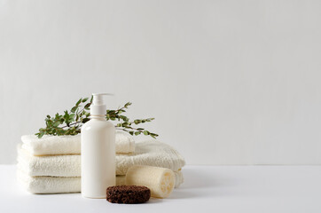 Fototapeta na wymiar Set for spa procedures for body care, kicks. A stack of pure cotton milk-colored towels, a bottle of cream, lotion, washcloth and peeling for foot care on a light background, selective focus