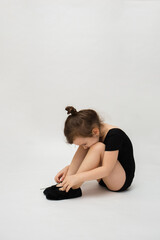 Fototapeta premium little gymnast girl sits on a white background with space for text