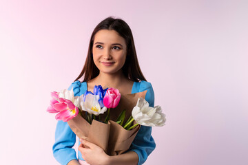 Gentle woman holding a bunch of multicolor tulips on neon pink background with side space for your advertisement. Romantic close up portrait o charming brunette girl looking into distance