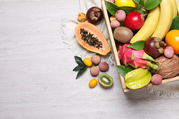 Crate and different exotic fruits on white wooden table, flat lay. Space for text
