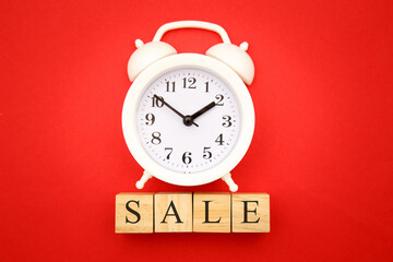 Sale and shopping concept. Four wooden cubes with SALE and alarm clock on red background.