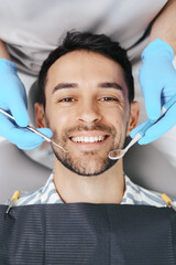 Smiling young man sitting in dentist chair while doctor examining his teeth