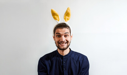 Man with rabbit ears. Charming young man with beard in shirt wearing Easter bunny costume. Persom with hare ears smiles big smile. Creative banner for celebration of Easter.